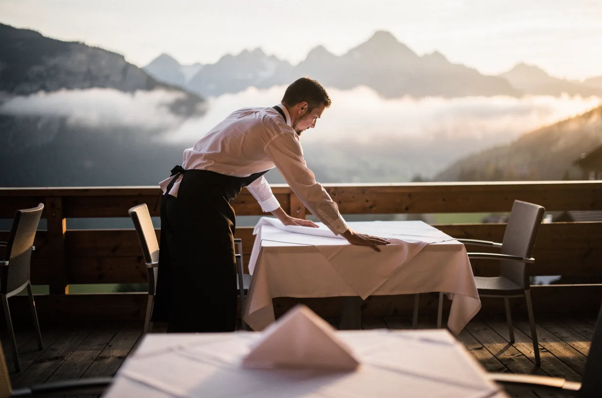 Serveur dressant une table sur la terrasse d'un hôtel de montagne au lever du jour